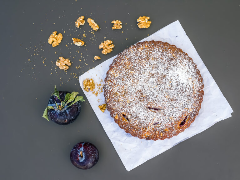 Plum cake with walnuts on white paper over a black background